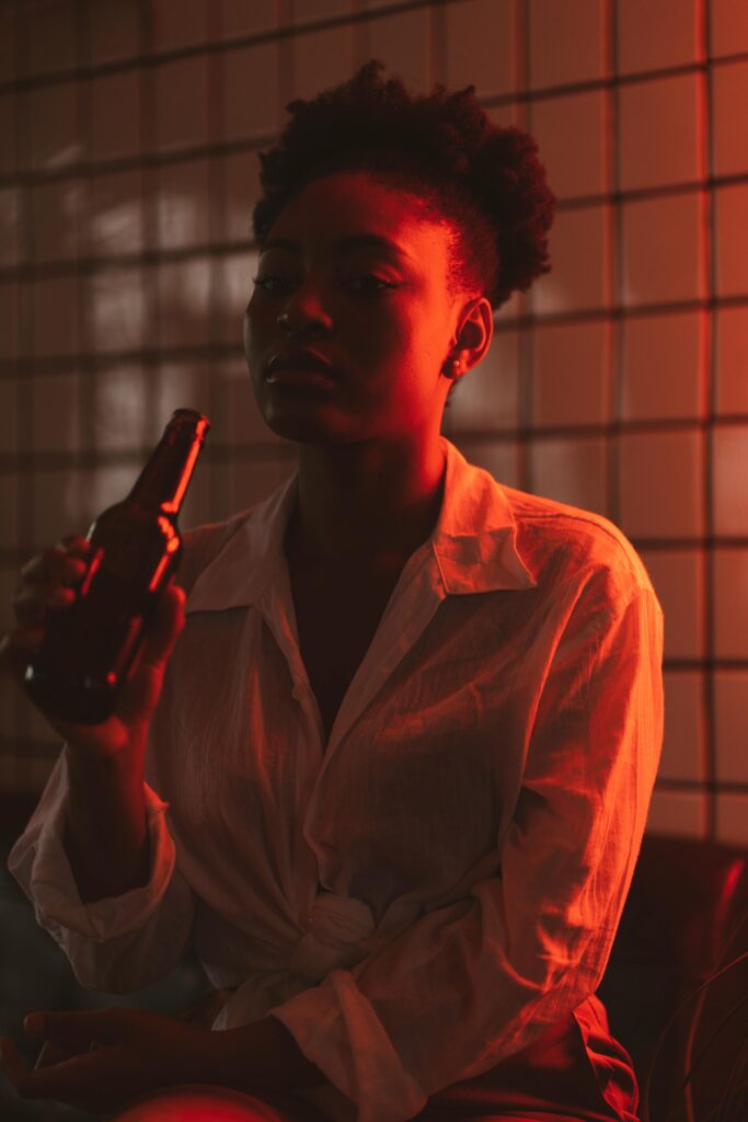 pexels-photo-5055808-5055808 A fashionable woman enjoys a beer indoors under soft red lighting, creating a relaxing evening mood.
